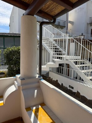 A white staircase with metal railings leading to an upper level, a beige pillar, and a yellow and white tiled floor. - Residence Mendolita (Lipari)