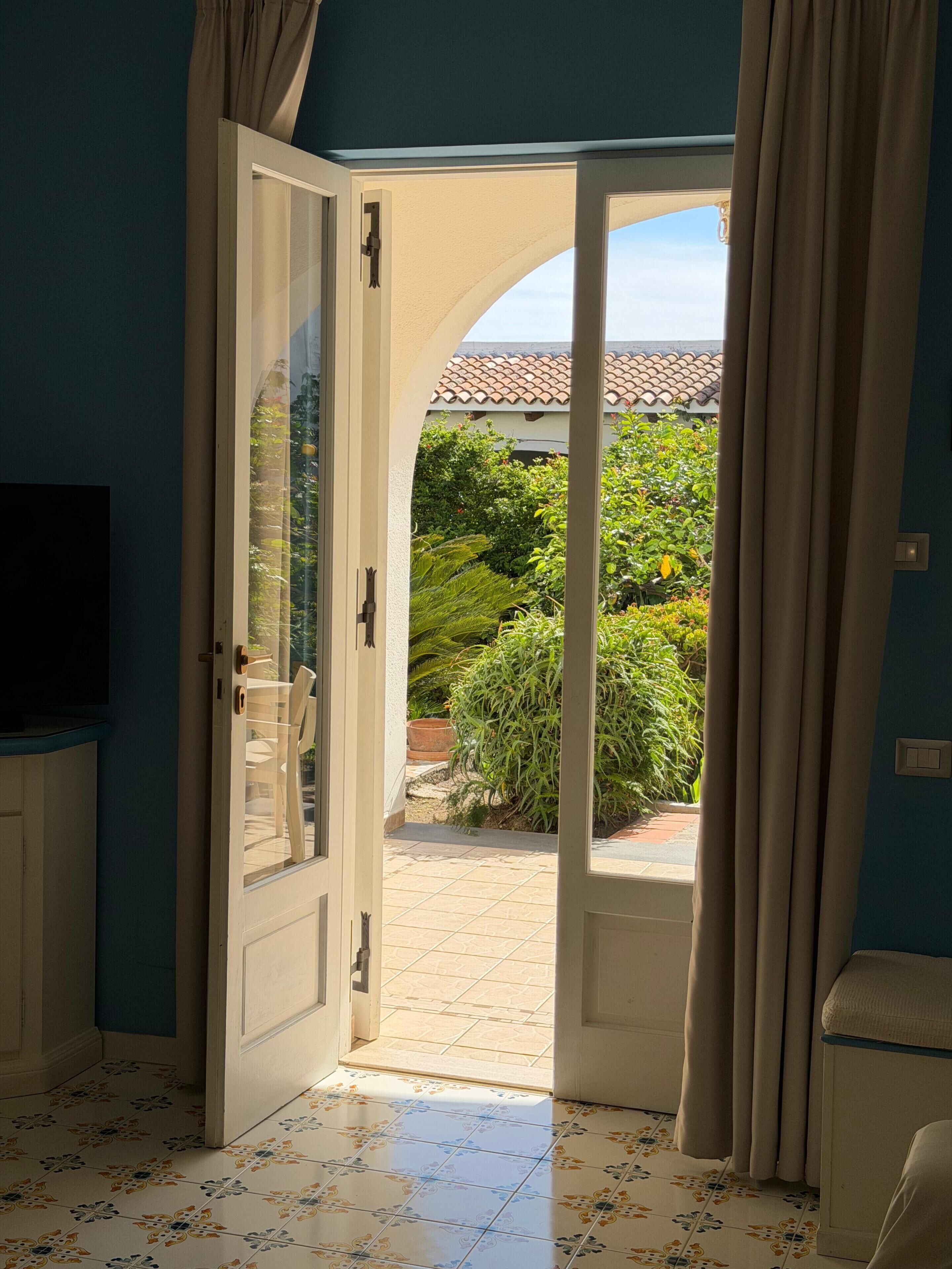 An open door leading to a tiled patio with a view of greenery and a tiled roof.