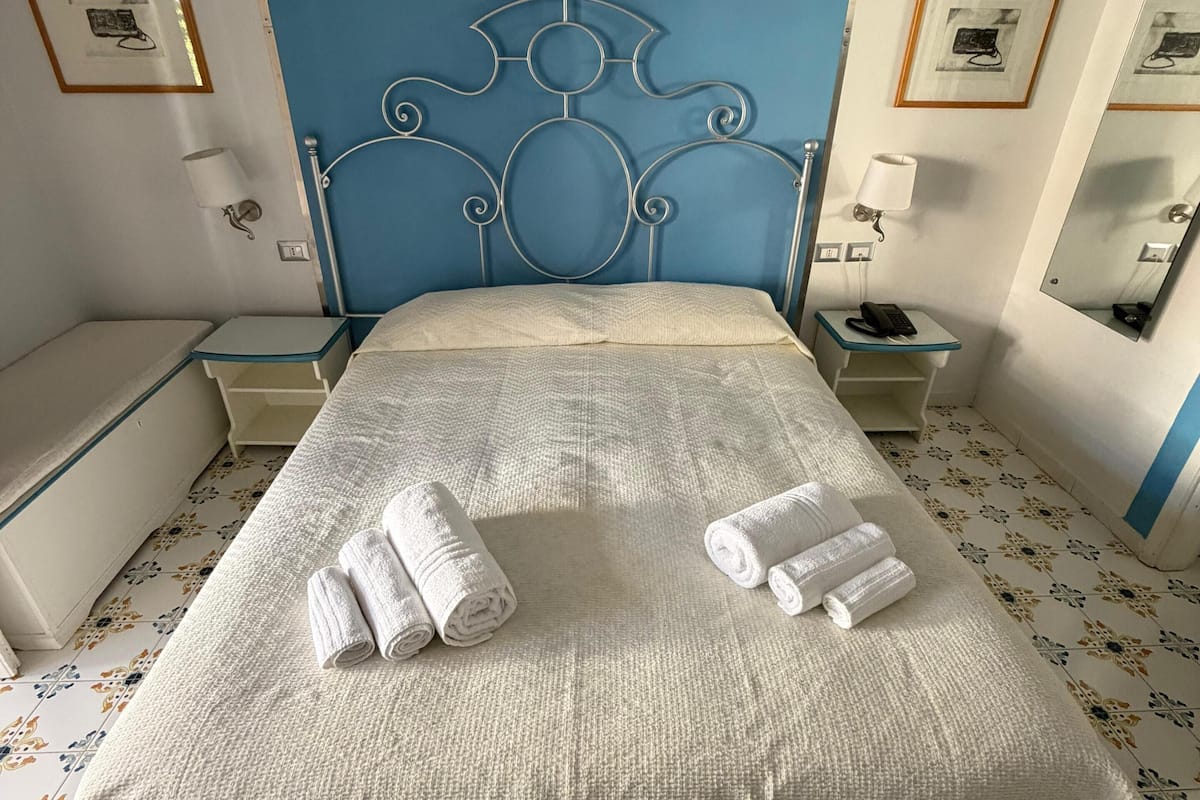 Una cama con cabecera, dos mesitas de noche, un espejo y una pared con detalles azules.