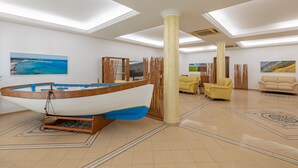 A spacious room with a large wooden boat model, a television, and yellow armchairs. - Hotel Sabbia D'Oro (San Vito Lo Capo)
