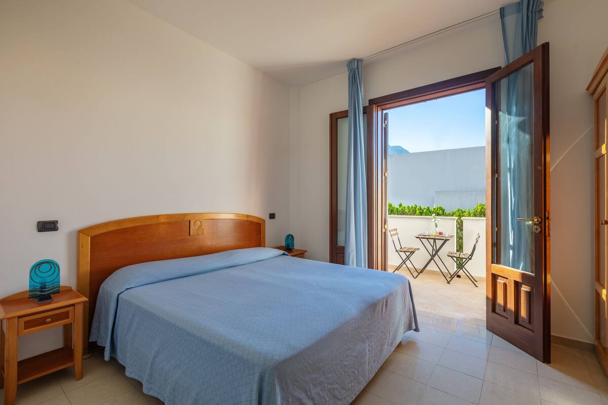 Een hotelkamer met een bed, nachtkastje, een klein tafeltje en uitzicht op het balkon.