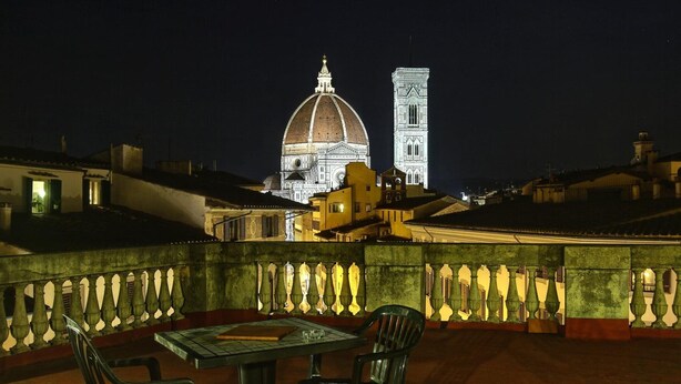 Terraza en la azotea con una mesa y sillas, con vistas a un edificio histórico con cúpula y torre.