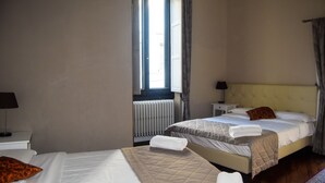 Habitación de hotel con dos camas, una ventana con cortinas, un radiador y una mesita de noche con lámpara.