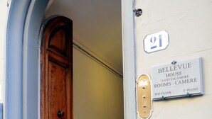 En trædør med messinggreb, et skilt der angiver værelsesnummer 21, og en plade med teksten "BELLEVUE HOUSE APT. CAMERLE TOP FLOOR 3RD PIANO".