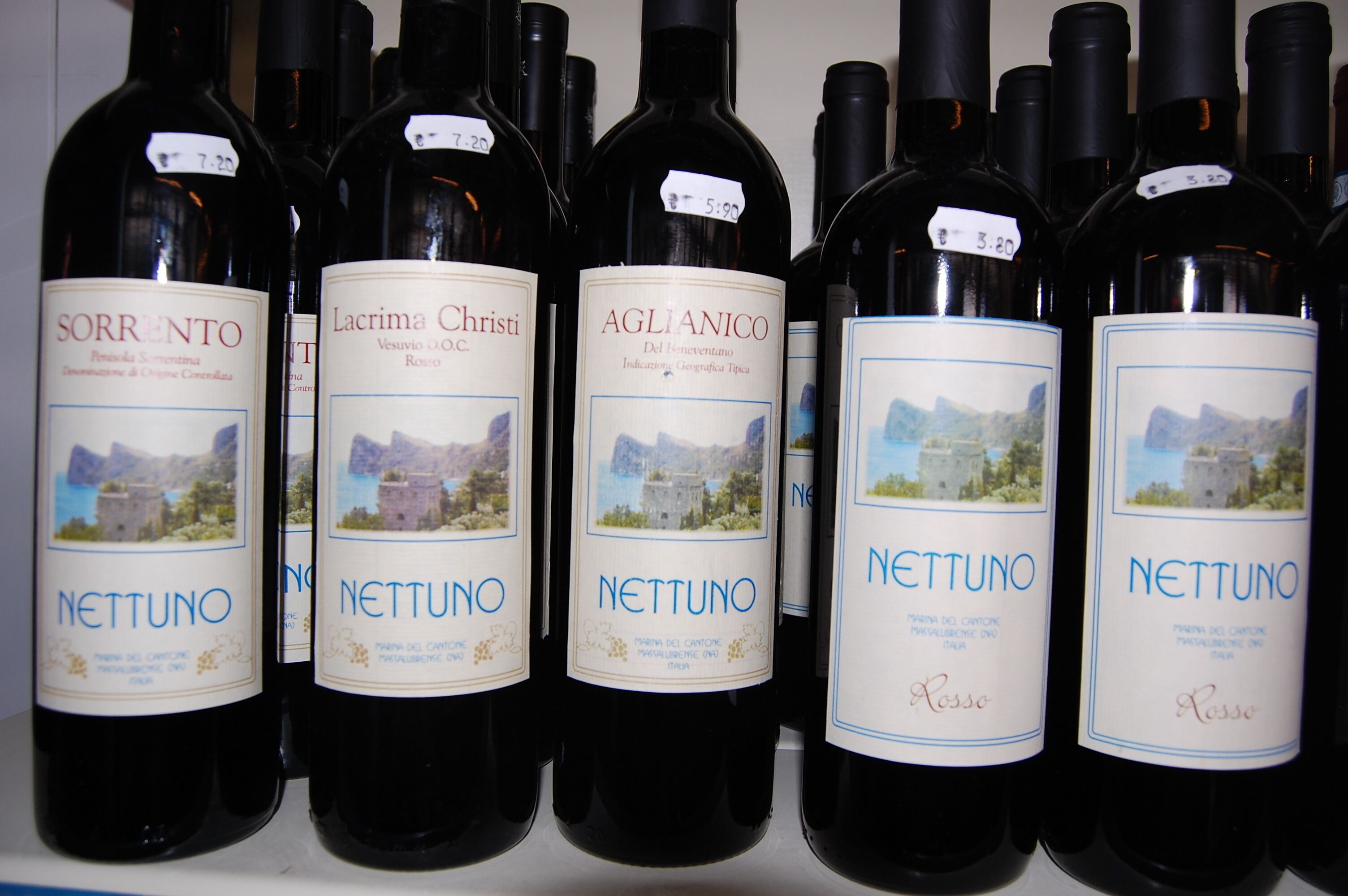 Una fila di bottiglie di vino con etichette che indicano diverse tipologie e le loro origini.