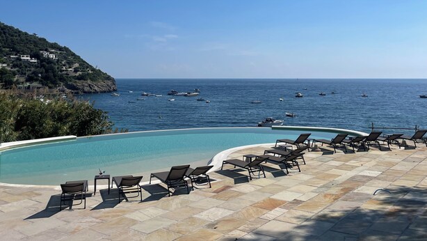 Zona de piscina con sillones de descanso y vista al mar.