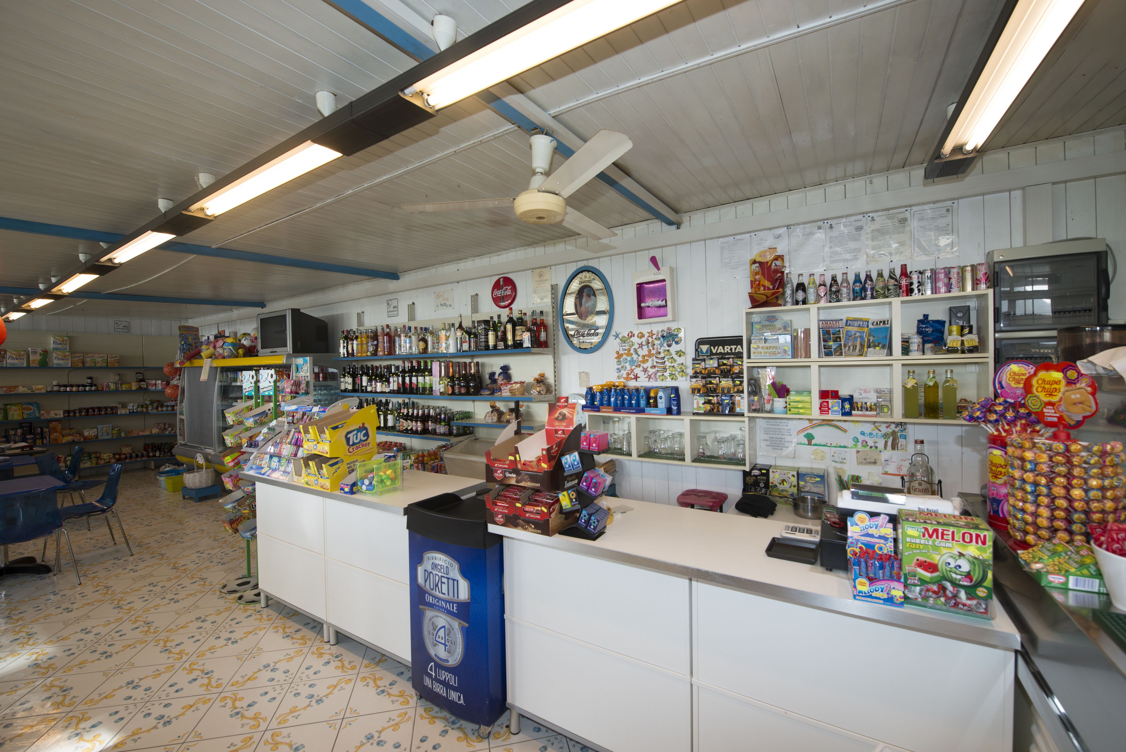 L’intérieur d’un magasin, avec un comptoir, des étagères remplies de divers produits et une poubelle.