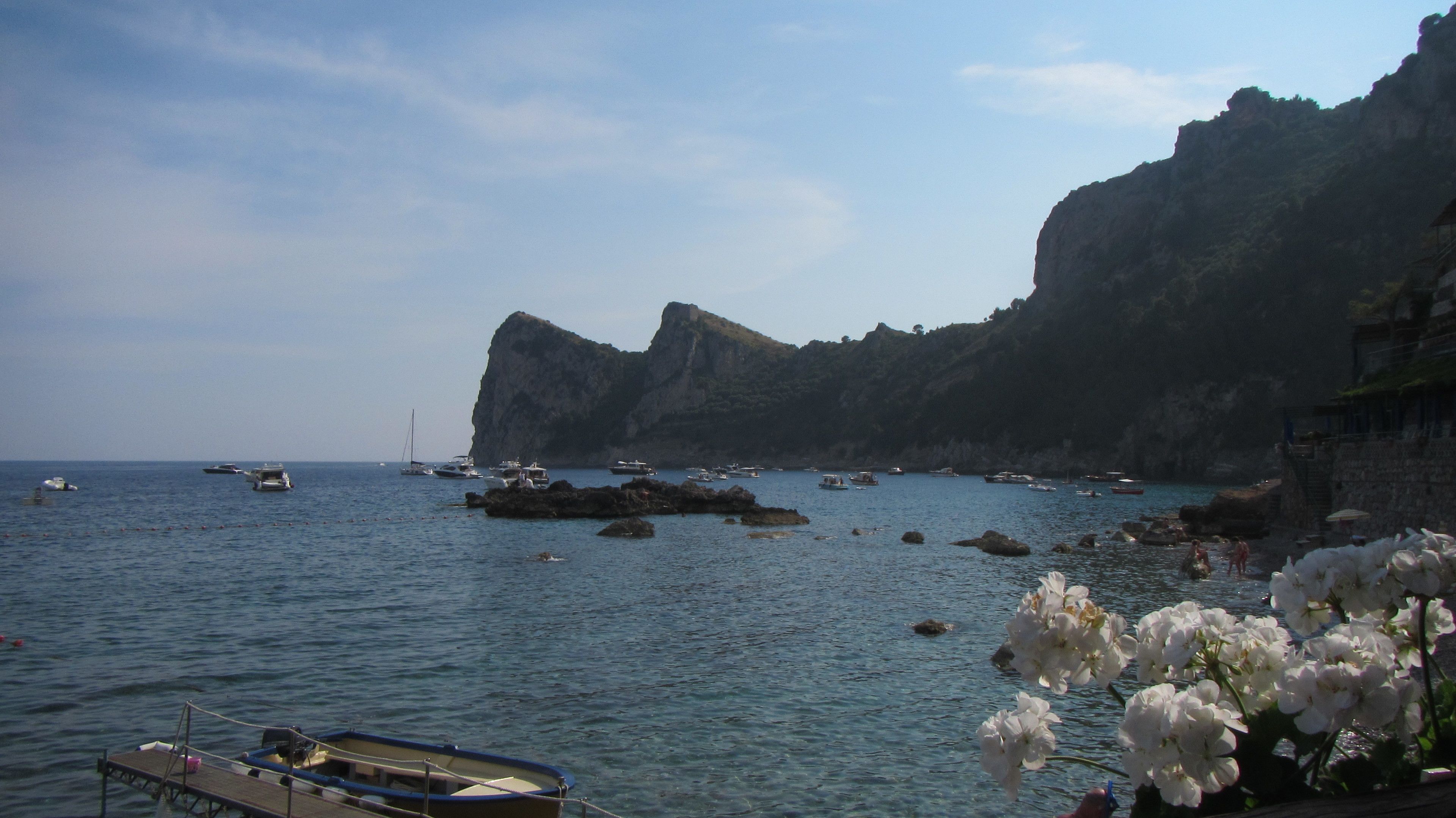 A coastal scene with boats, rocky cliffs, and a clear sky.