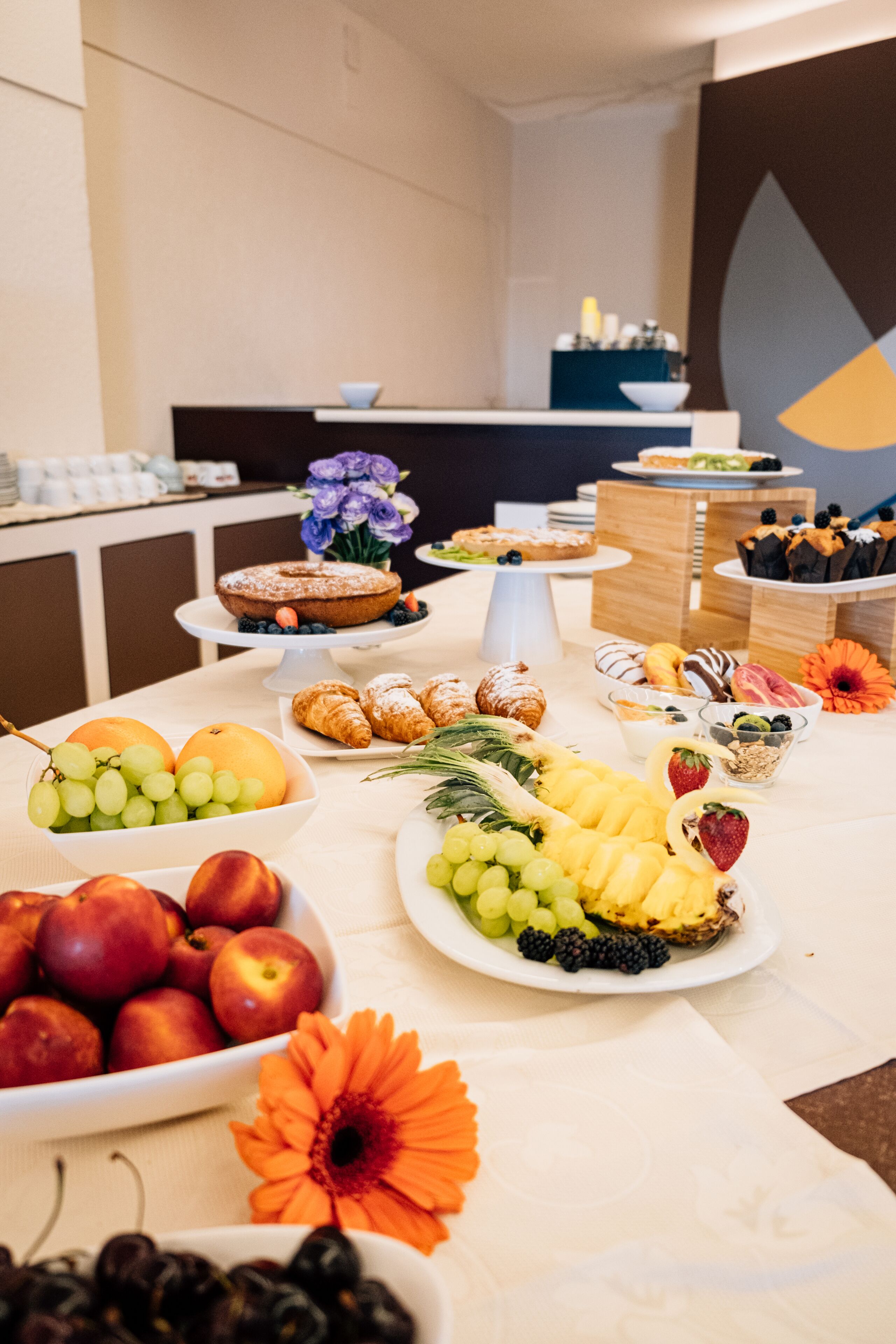 Une table de buffet garnie de divers fruits, de pâtisseries et d’un vase rempli de fleurs.