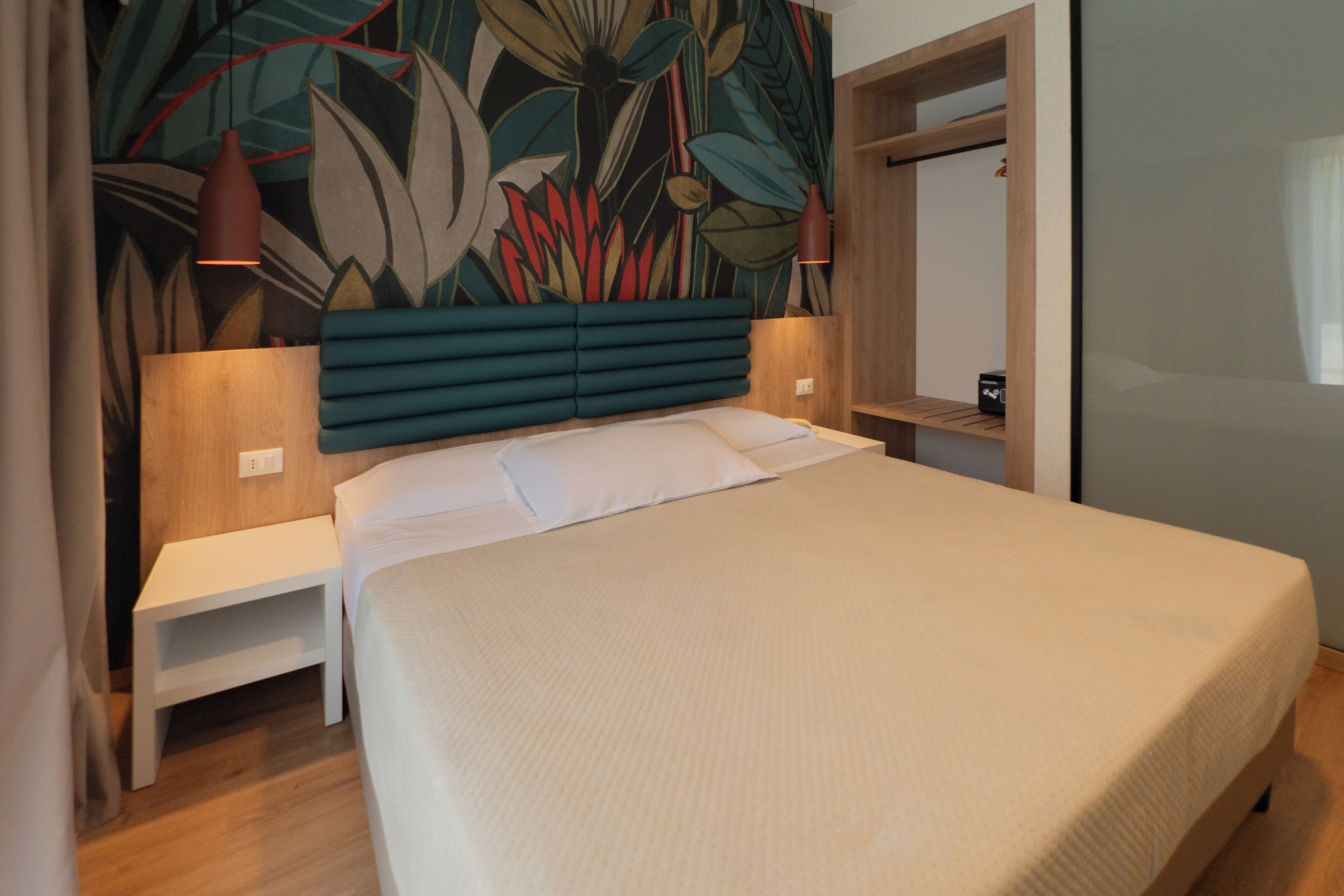 Un dormitorio moderno con una cama grande, cabecera decorada con un mural floral, mesitas de noche y una mesita auxiliar.