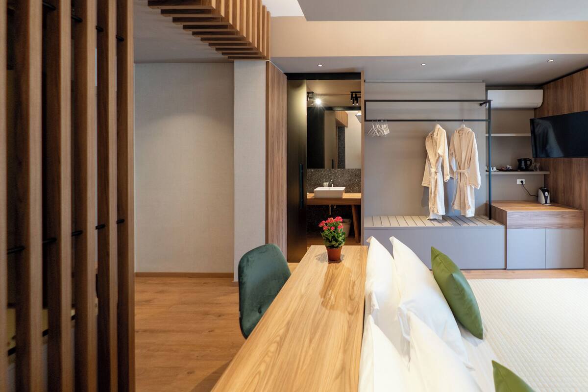 Ein modernes Hotelzimmer mit einem Holztisch, einem Bett mit weißer Bettwäsche, einem grünen Sessel und einem kleinen Blumentopf.