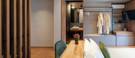 A modern hotel room with a wooden dining table, a bed with white bedding, a green chair, and a small potted plant.