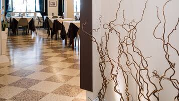 A hotel lobby with a checkered floor, a glass railing with decorative branches, and tables and chairs arranged for dining.