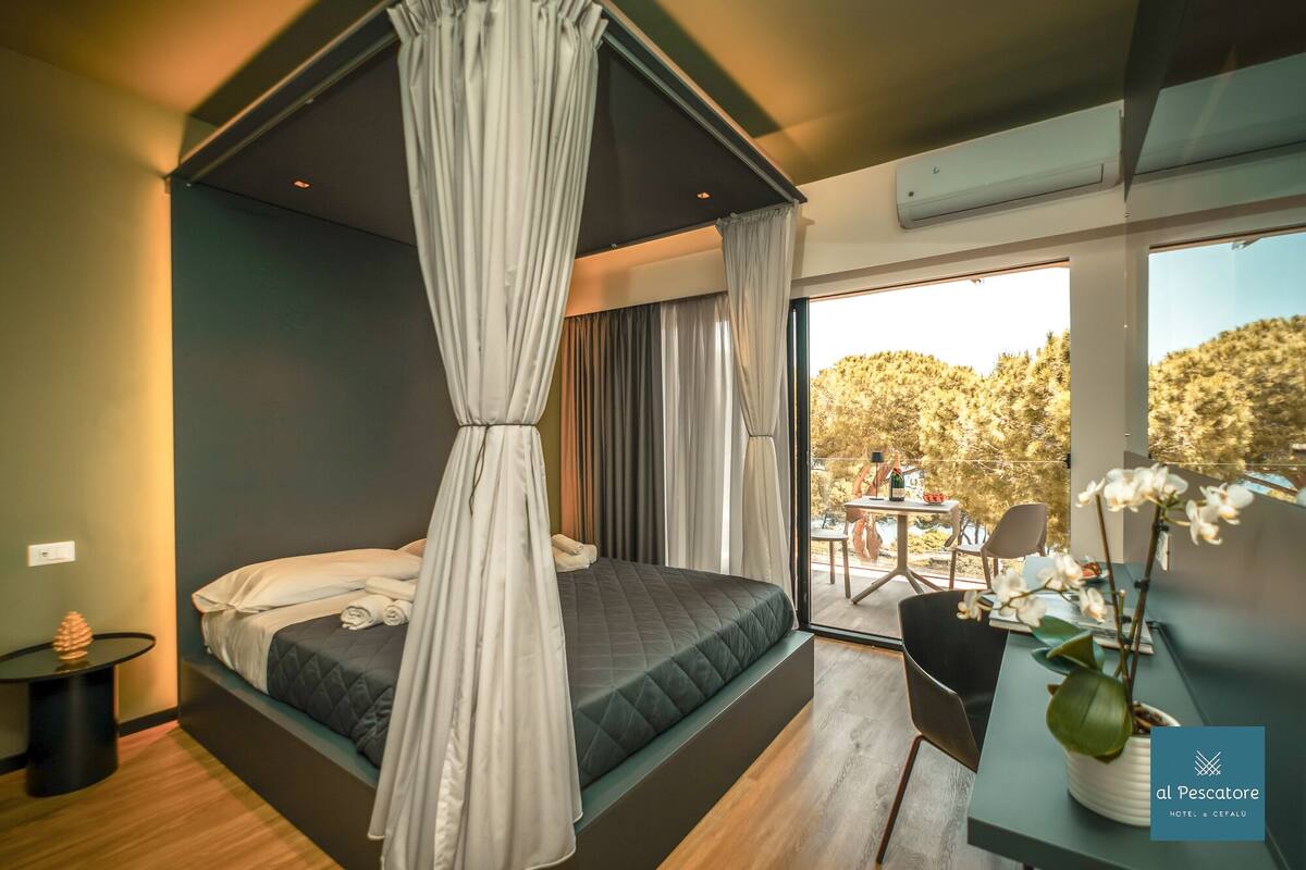 Ein modernes Schlafzimmer mit einem großen Bett, einem Balkon mit Tisch und Stühlen und Blick auf Bäume.