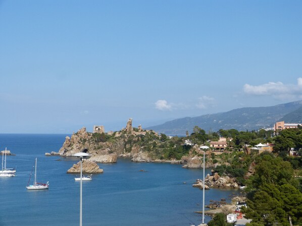 Un pueblo costero con terreno rocoso, un faro y barcos en el agua.