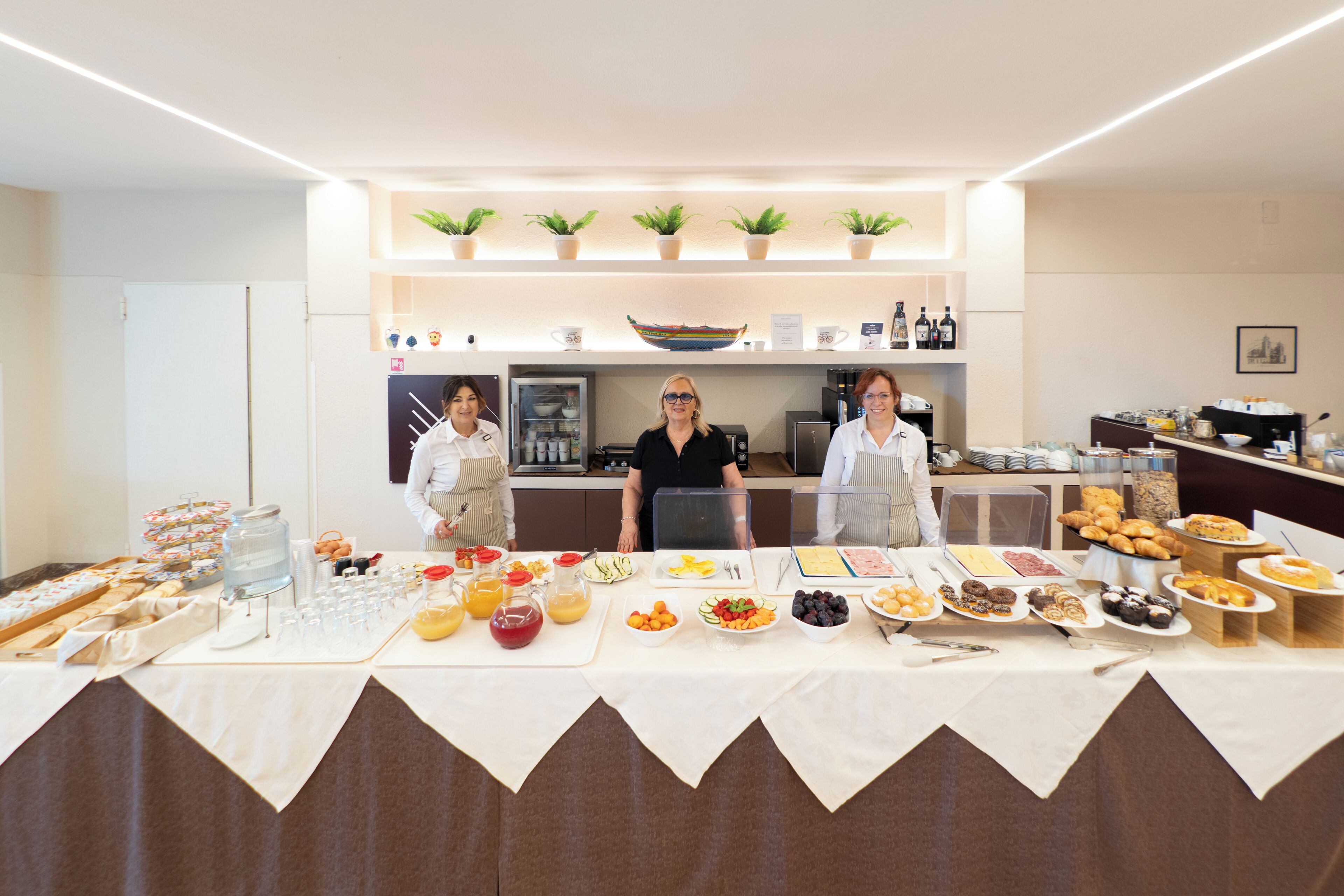 Montaje tipo bufé con diversas opciones de comida y bebidas, incluyendo frutas, pasteles y una estación de café.