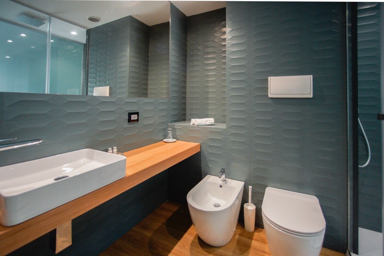 A modern bathroom with a wooden vanity, a large sink, a bidet, and a toilet.