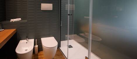 A modern bathroom with a bidet, toilet, and glass shower enclosure.