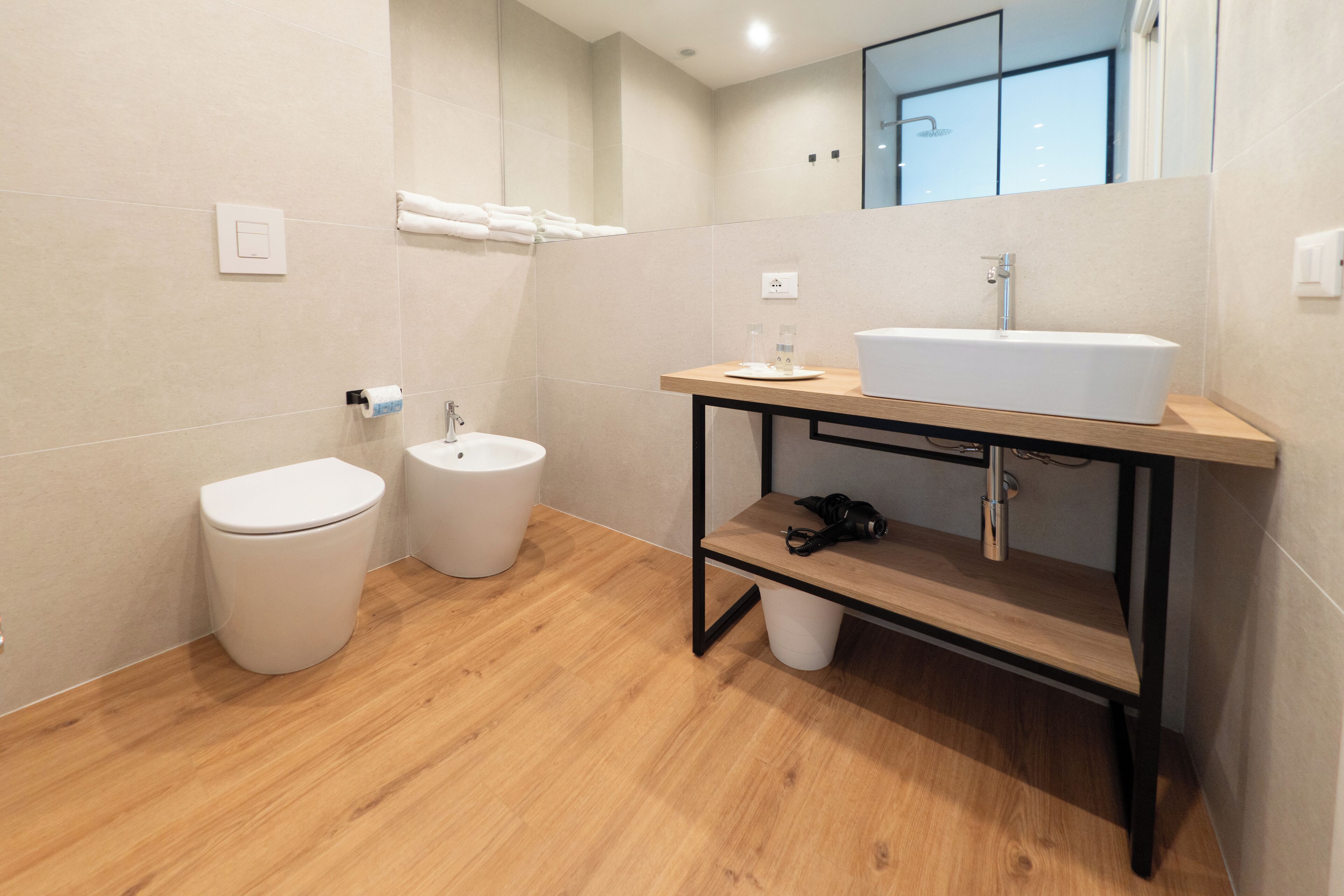 A modern bathroom with a toilet, bidet, and a sink on a wooden vanity.