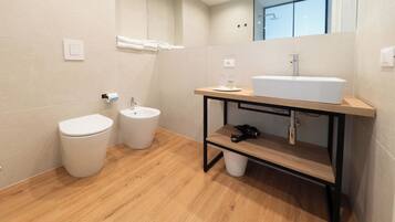 Un baño moderno con inodoro, bidé y lavamanos sobre un mueble de madera.