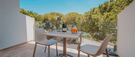 A balcony with a table, two chairs, a bottle of champagne, and a bowl of fruit.