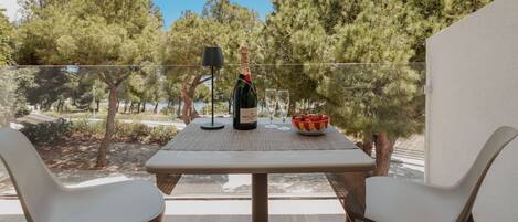 A balcony with a table set for two, a bottle of wine, and a bowl of fruit.