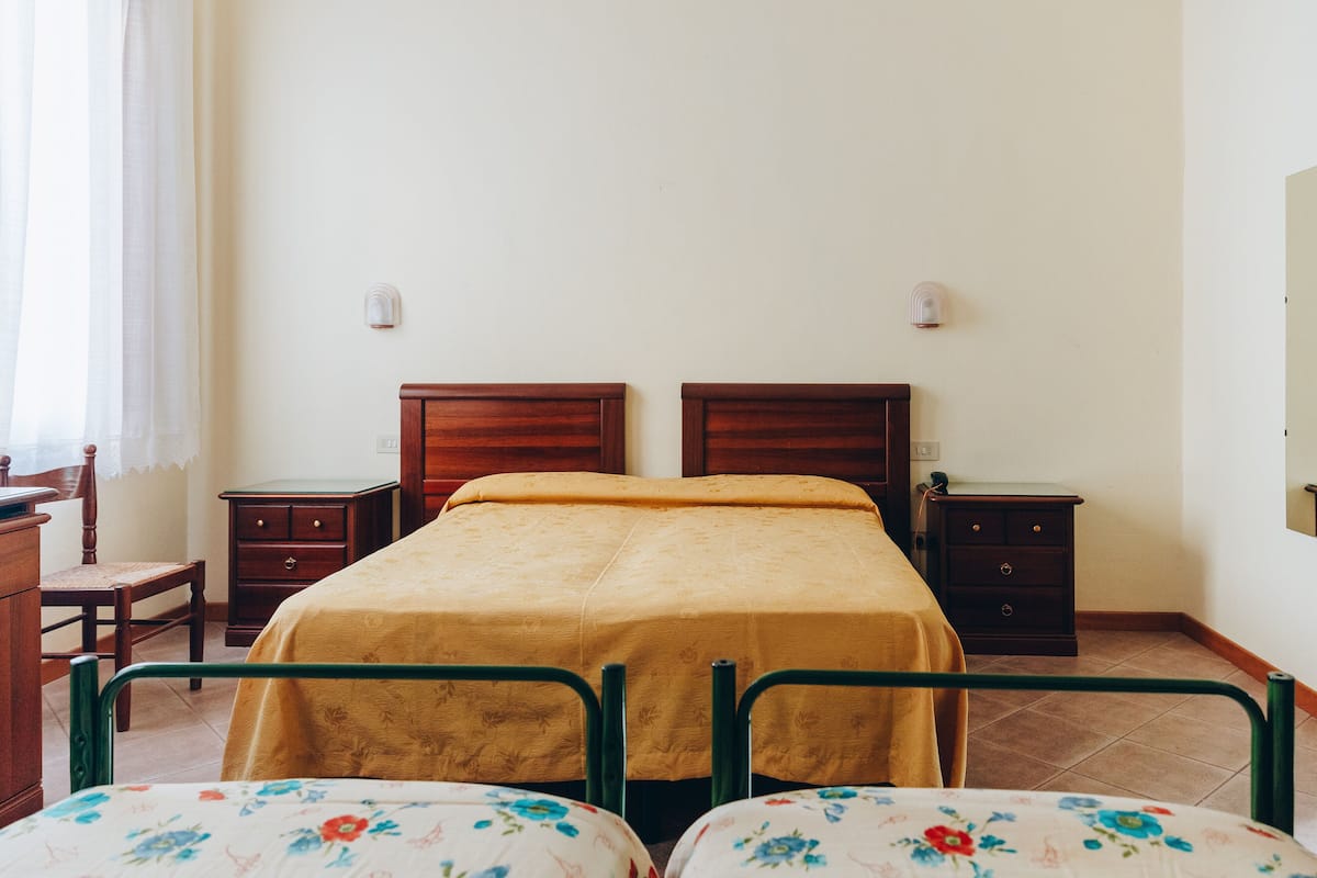 Un dormitorio con dos camas, cabeceros de madera, una mesita de noche, un aparador y una silla.