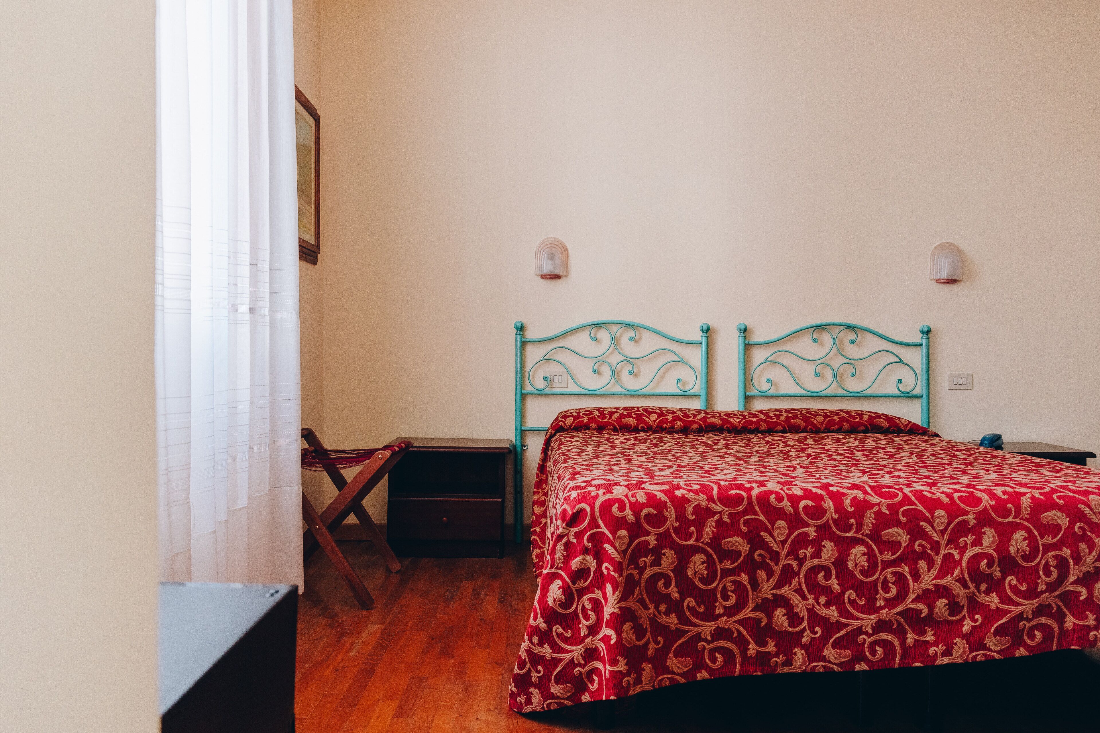 A bedroom with a bed, a nightstand, a chair, and a window with curtains.