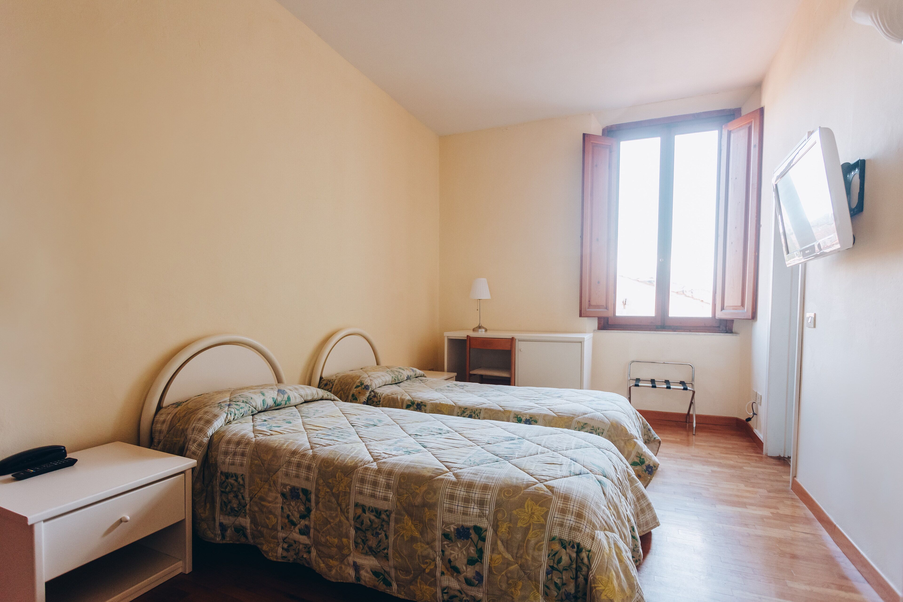A bedroom with two beds, a desk, a chair, and a TV on the wall.