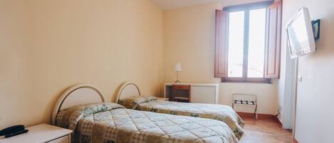 A bedroom with two beds, a desk, a chair, and a TV on the wall.