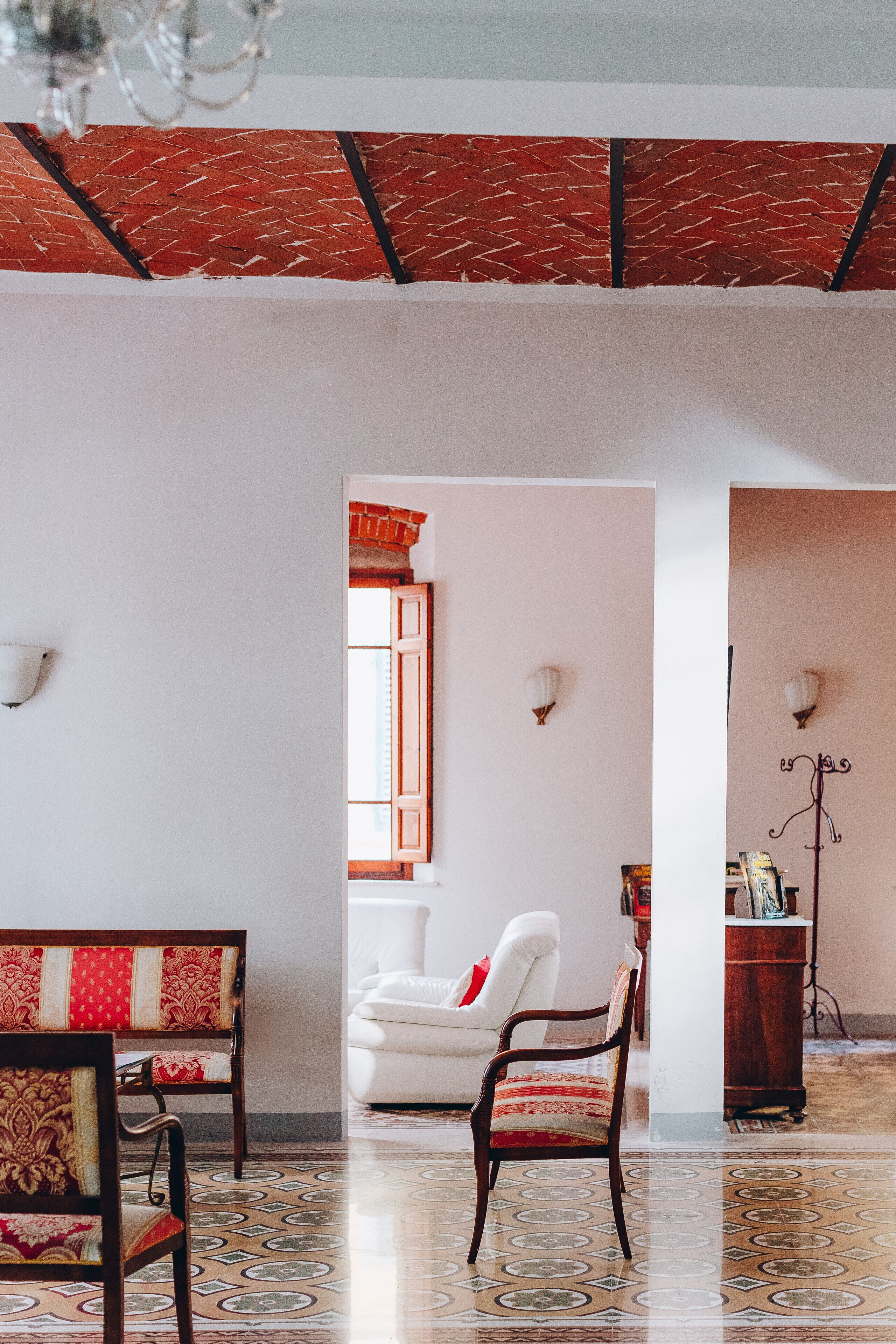 A room with a patterned floor, a white chair, a wooden bench, and a red and white patterned sofa.