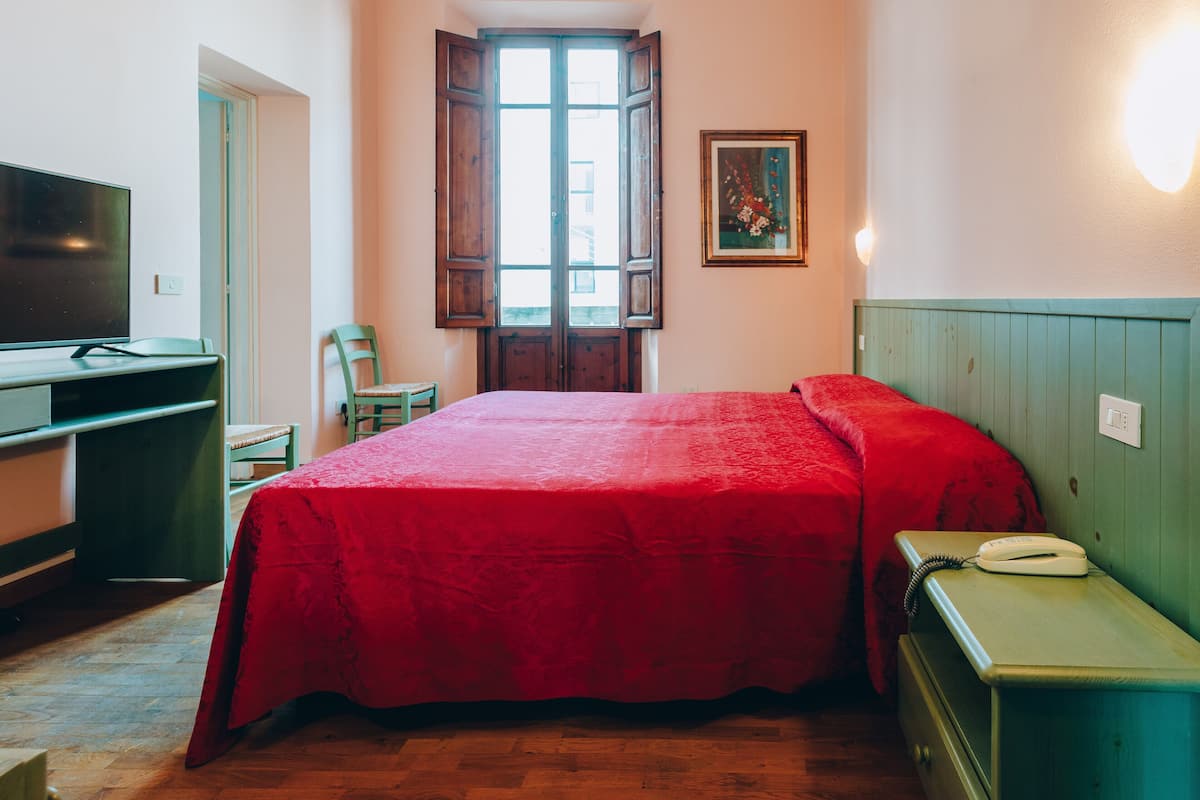 Un dormitorio con cama, escritorio, silla, televisor y ventana con persianas de madera.