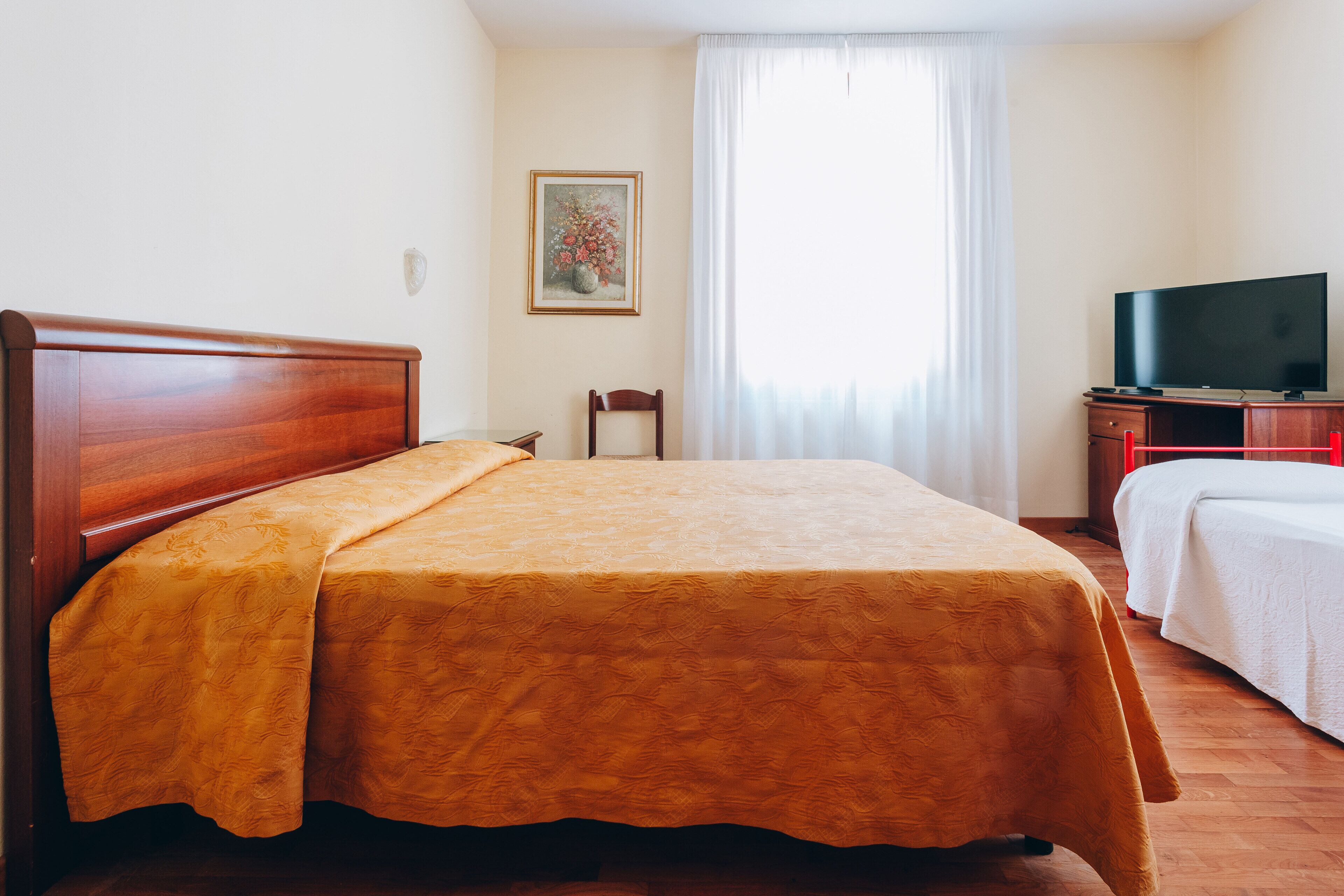 A hotel room with a wooden bed, a television on a wooden cabinet, and a window with curtains.