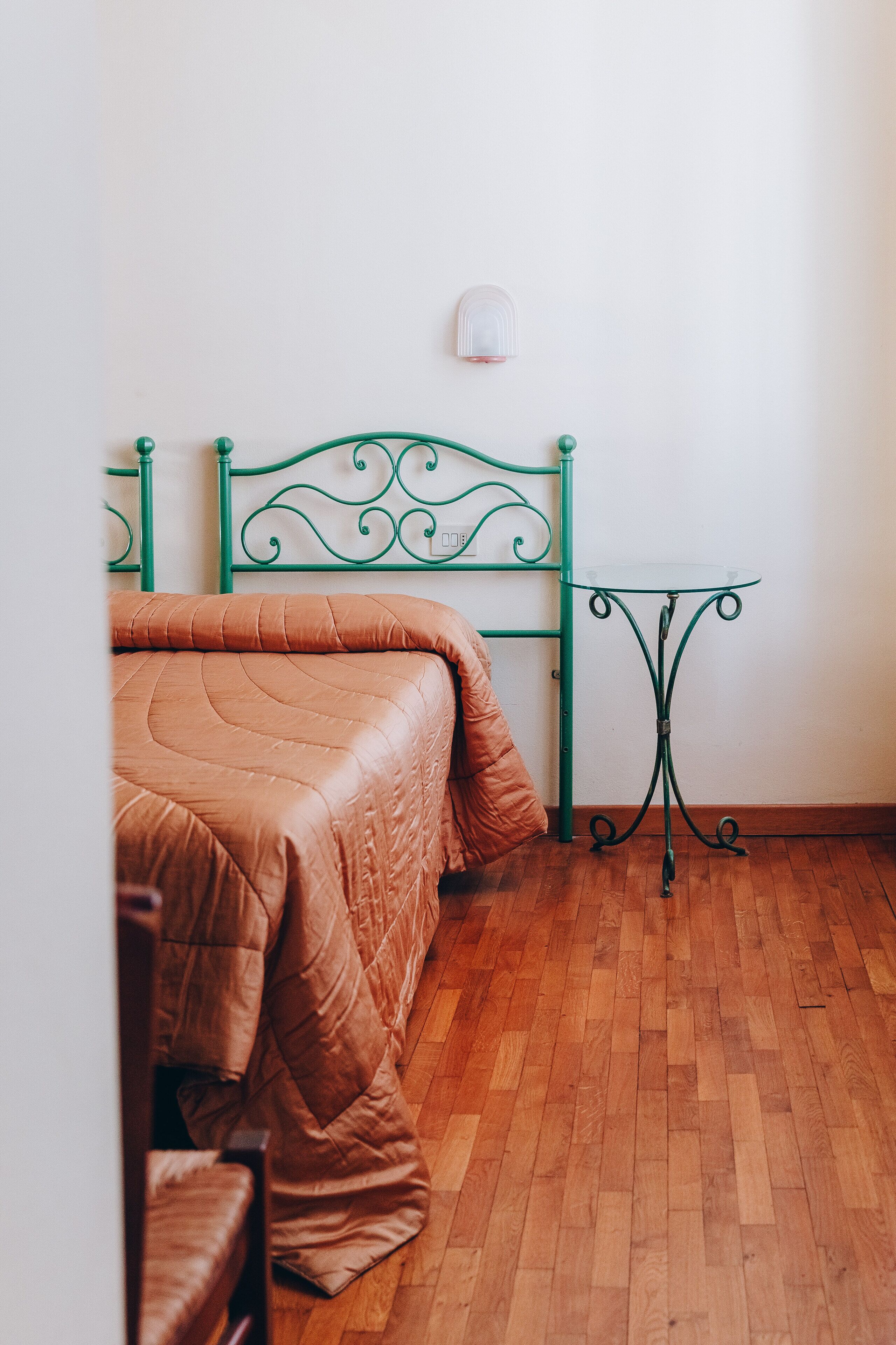 Une pièce avec un lit, une tête de lit en métal verte, une petite table et un mur blanc.
