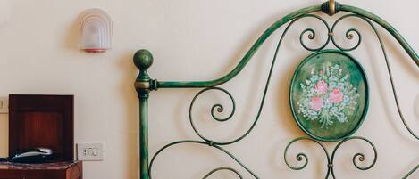 A bed with a green metal headboard, a wooden nightstand, and a wall-mounted light fixture.