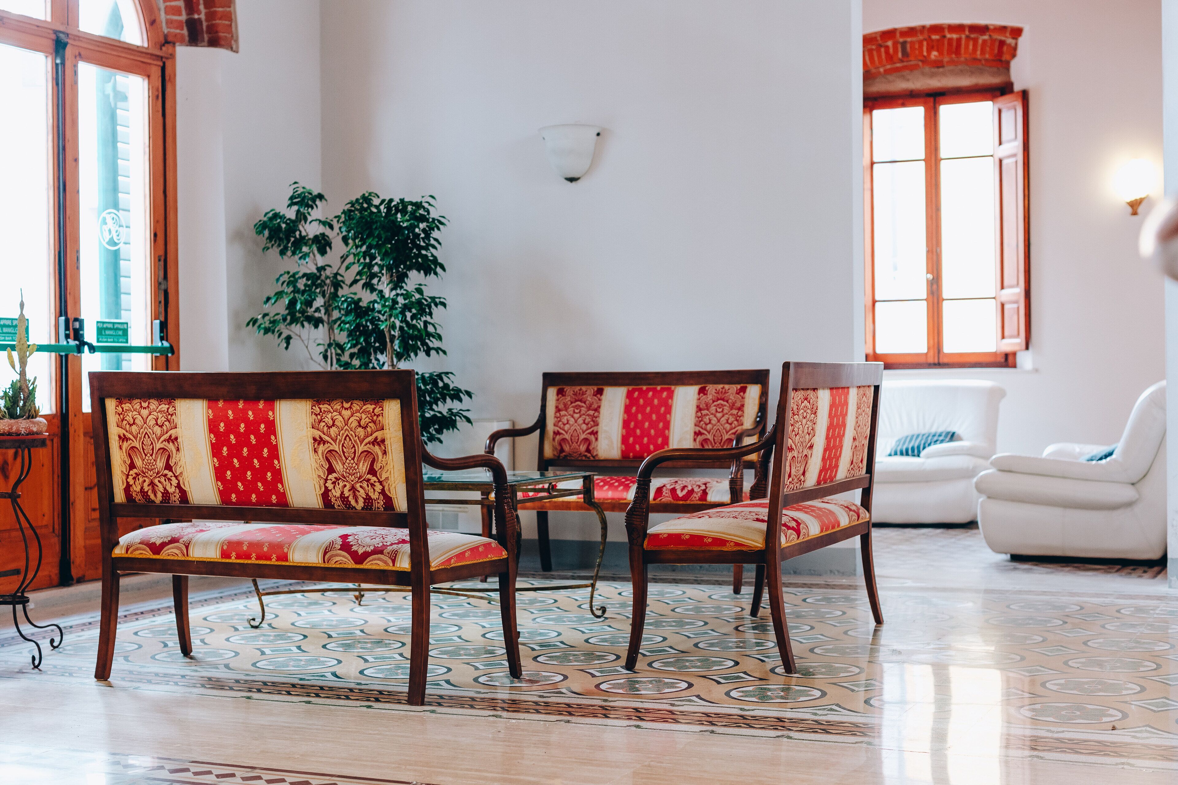 A room with a wooden sofa, matching chairs, a dining table, and a potted plant.