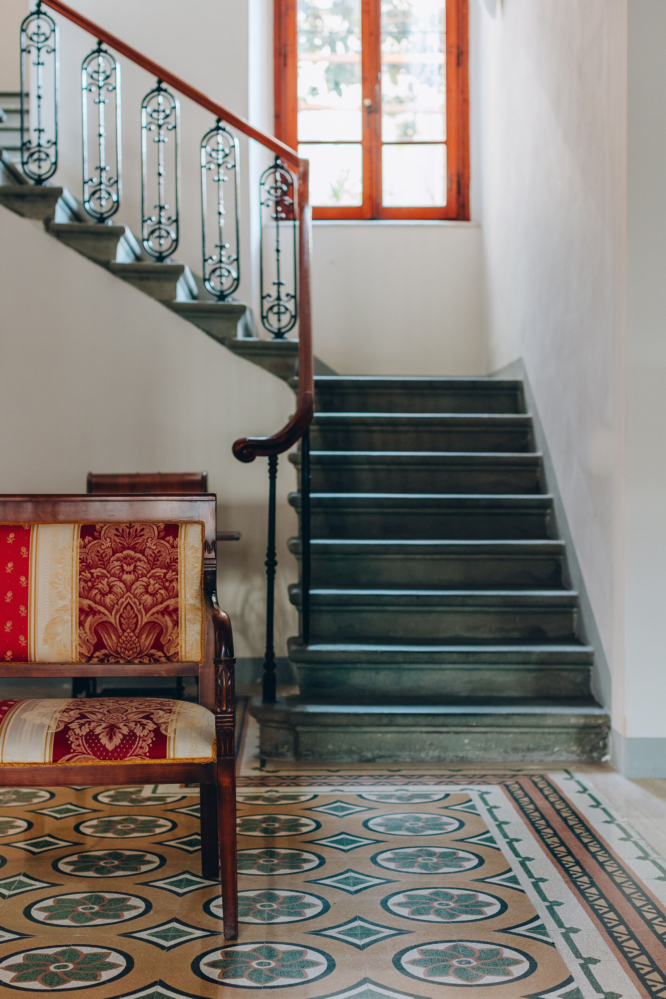 Una escalera con barandillas de metal decorativas, un banco de madera con cojín estampado y una alfombra con diseño.