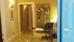 A spacious hallway with a checkered floor, a chandelier, a desk with a computer, and a large abstract painting on the wall. - Rubens (Catania)
