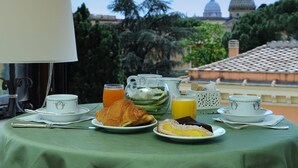 Une table de petit-déjeuner avec des croissants, un gâteau et du jus, le tout disposé devant une vue sur un bâtiment à coupole et des arbres.