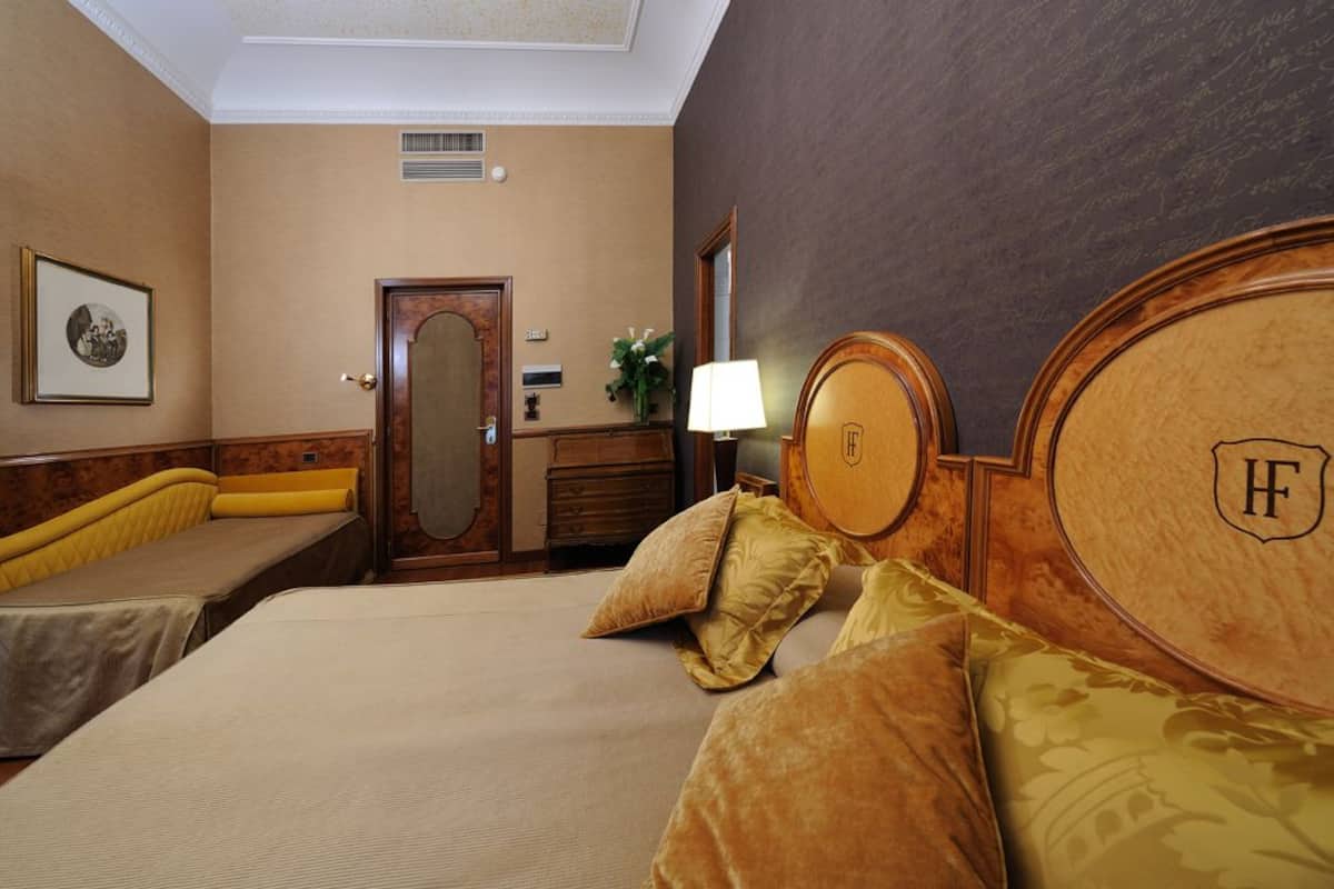 Ein Hotelzimmer mit einem großen Bett, zwei Nachttischen, einem Spiegel und einem kleinen Schreibtisch mit einer Lampe.