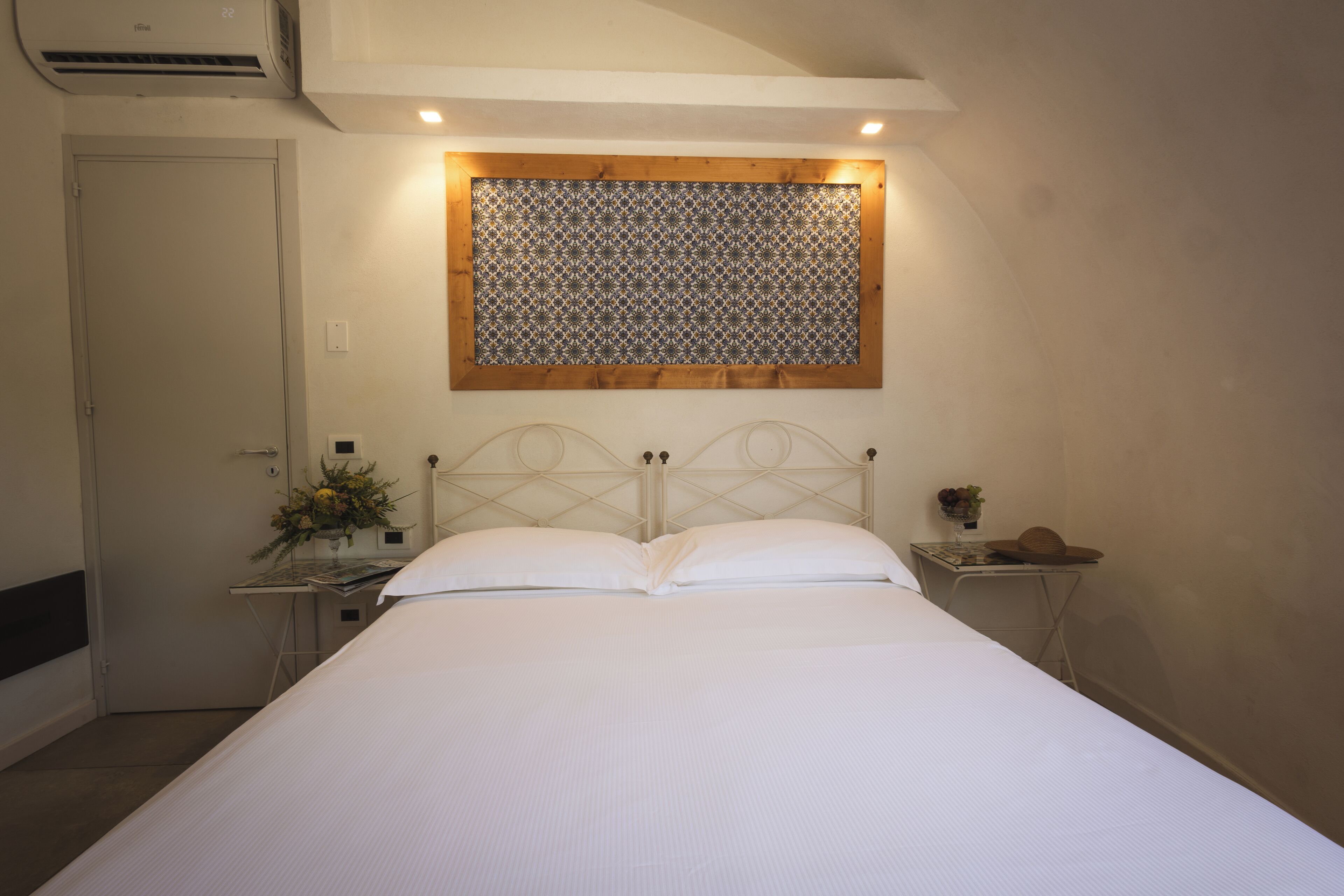 Een net opgemaakt bed met hoofdbord, een nachtkastje met een bloevas en een decoratief paneel aan de muur.