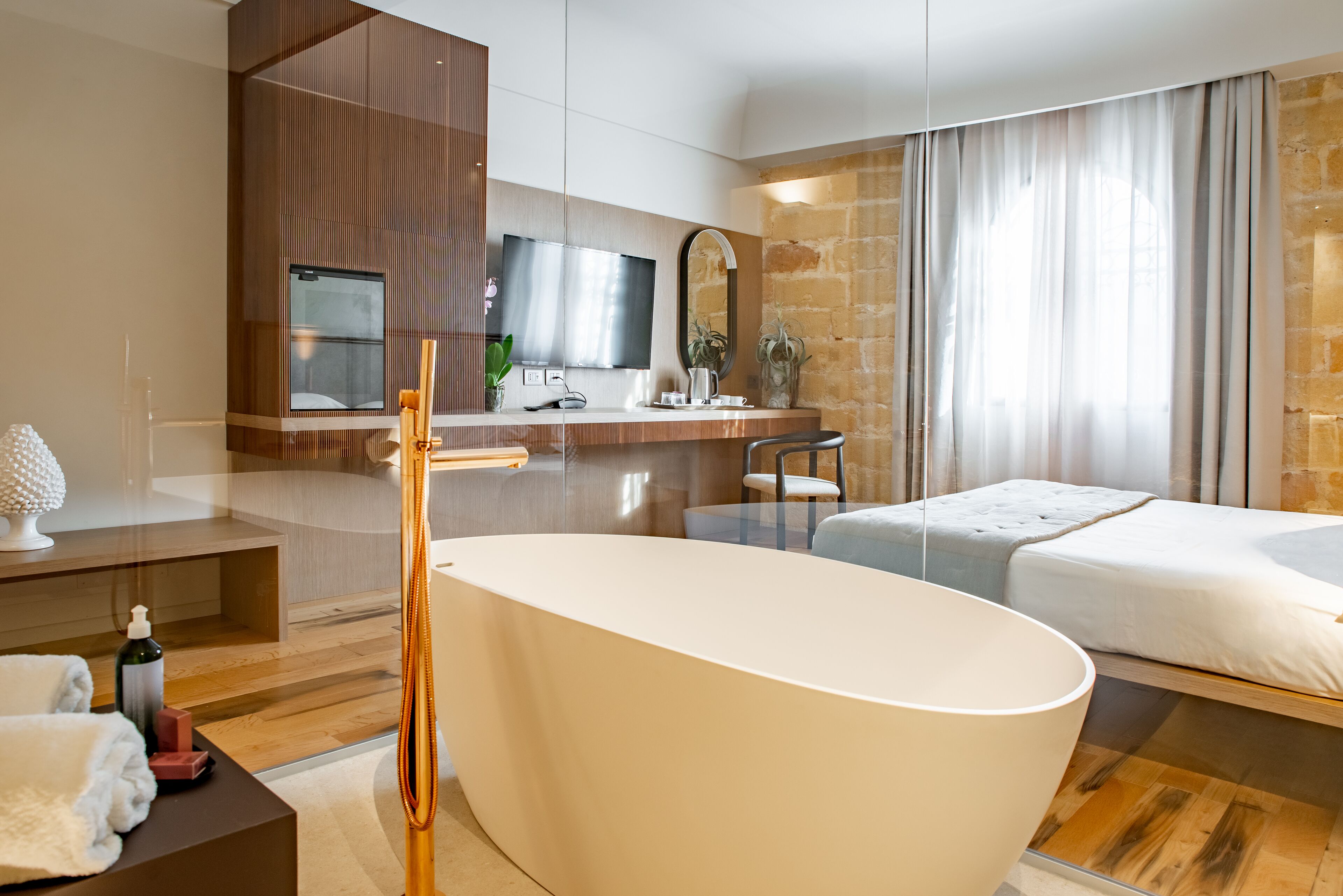 Ein modernes Hotelzimmer mit einer großen Badewanne, einem Holzwaschtisch, einem Flachbildfernseher und einer Wand mit Steinverkleidung.