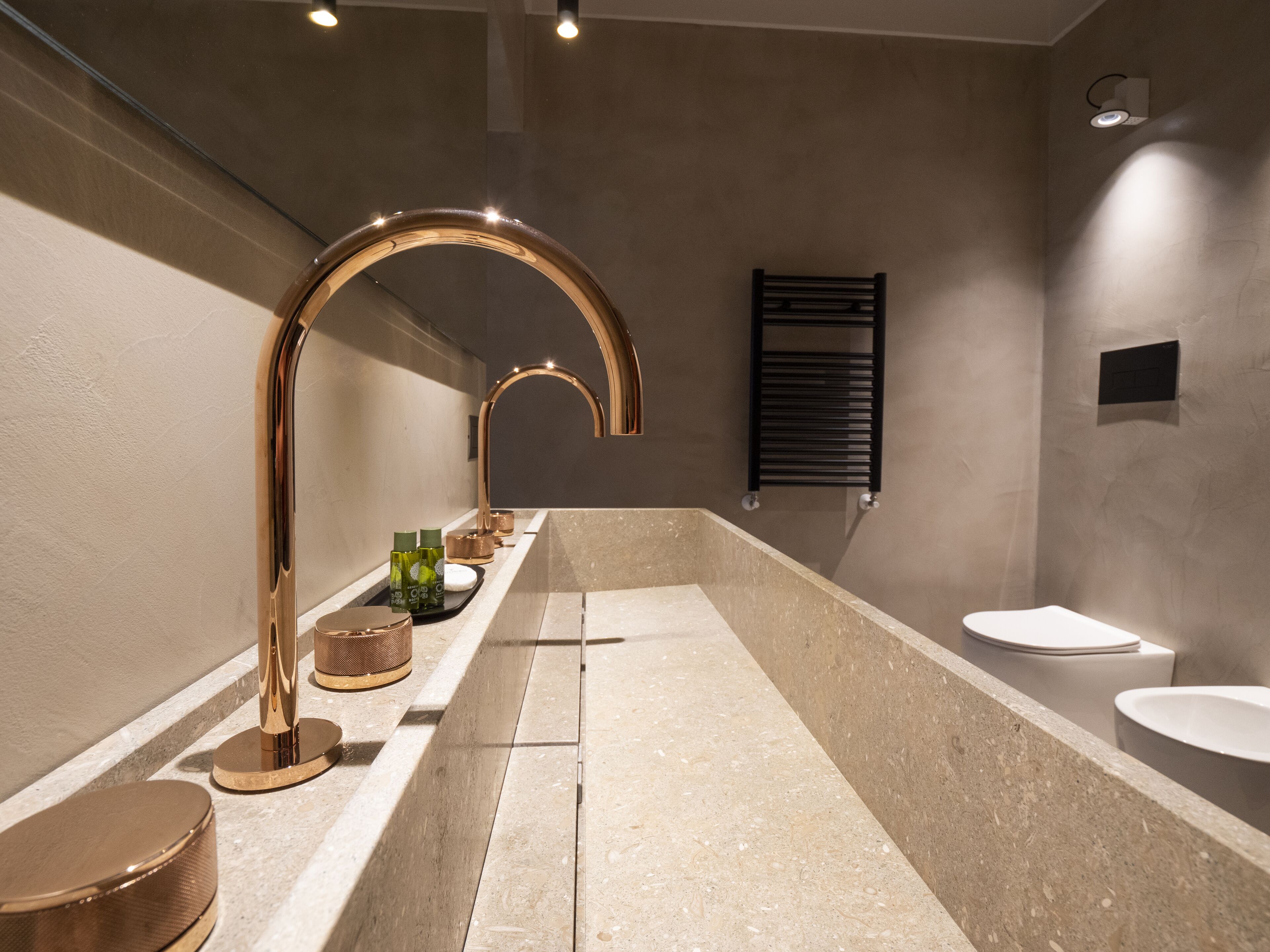 A modern bathroom with a large bathtub, a gold faucet, and a black towel rack.