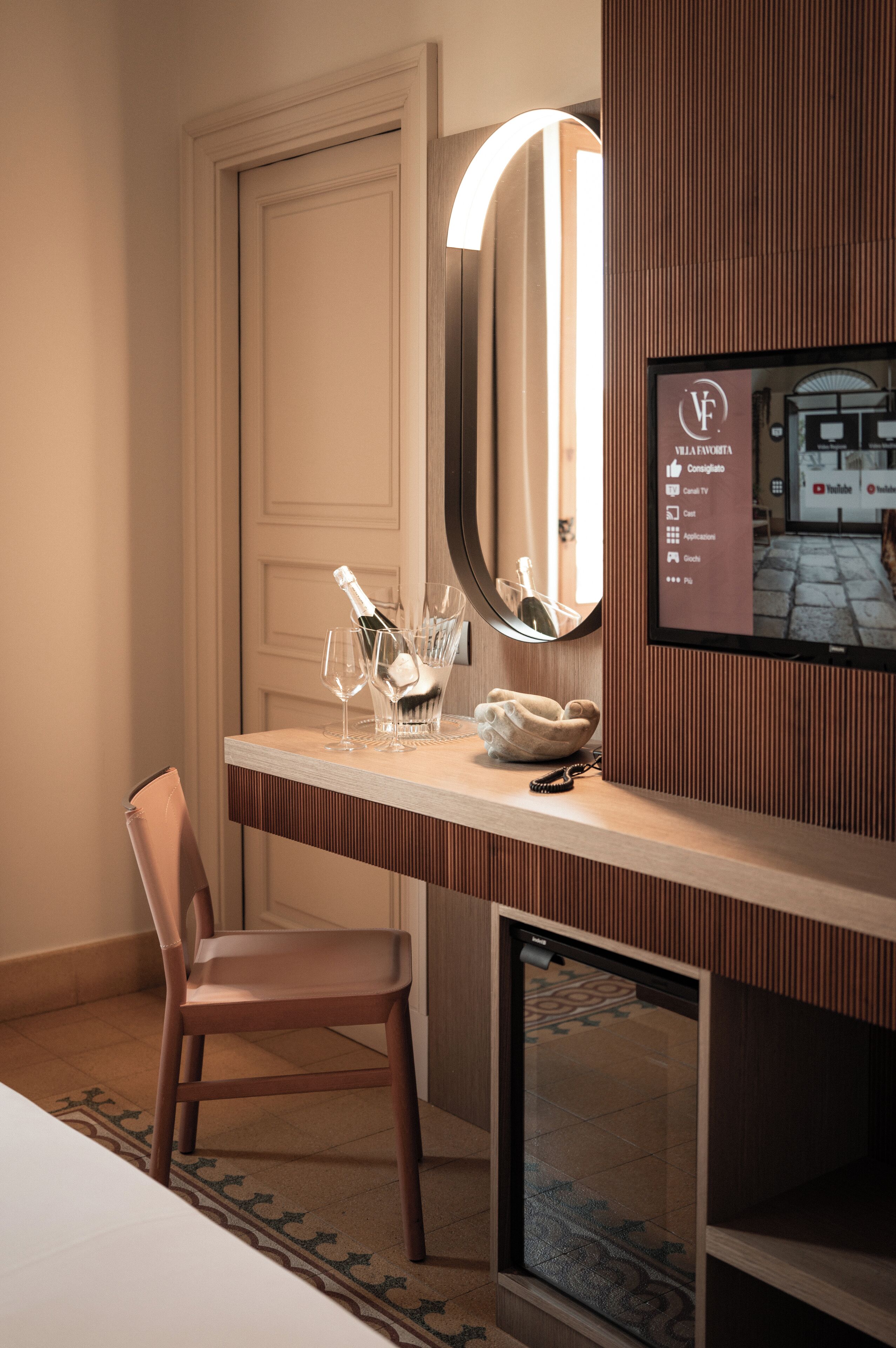 A hotel room with a wooden desk, a chair, a mirror, a TV, and a door.