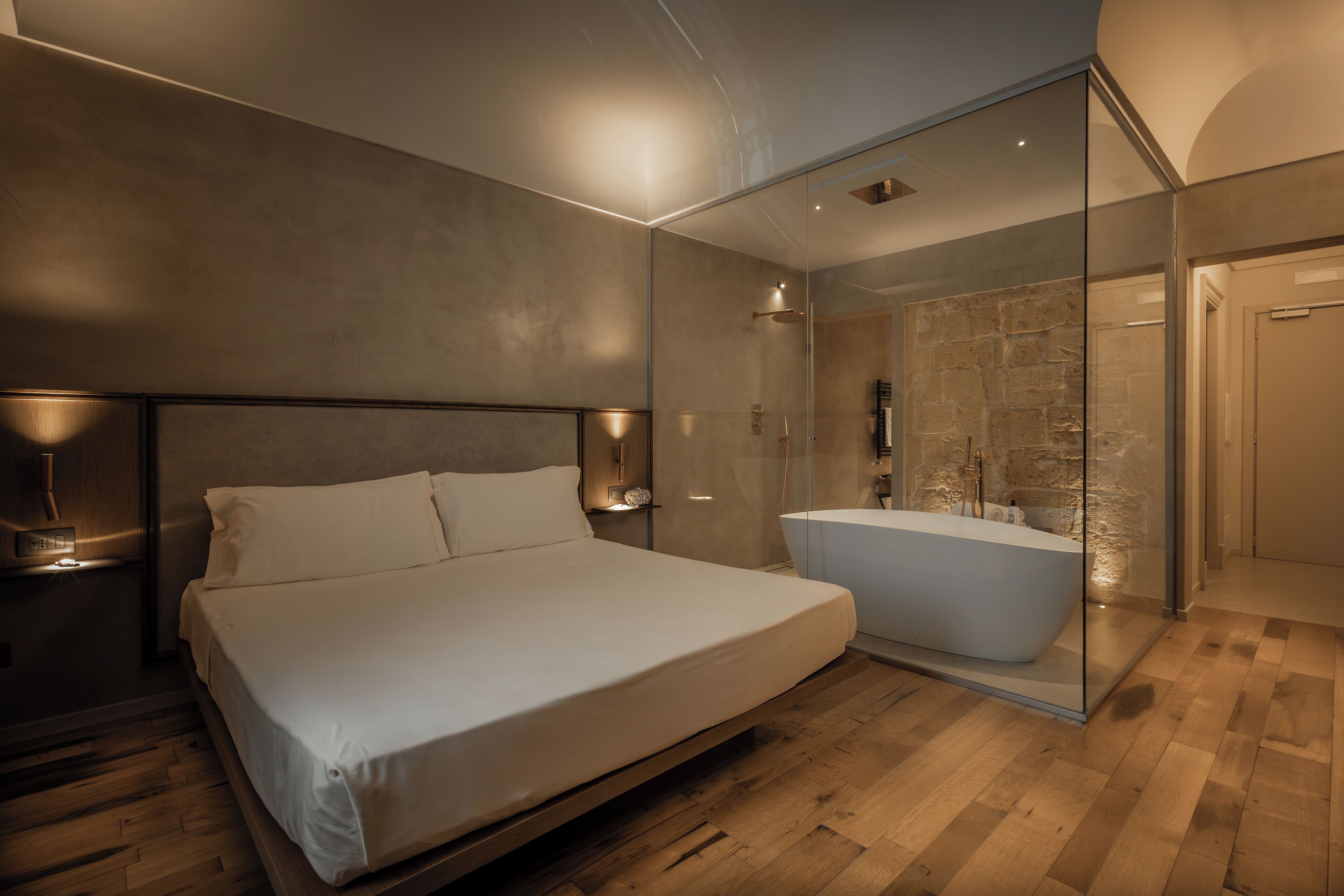 A modern bedroom with a large bed, a glass-enclosed shower, and a wooden floor.
