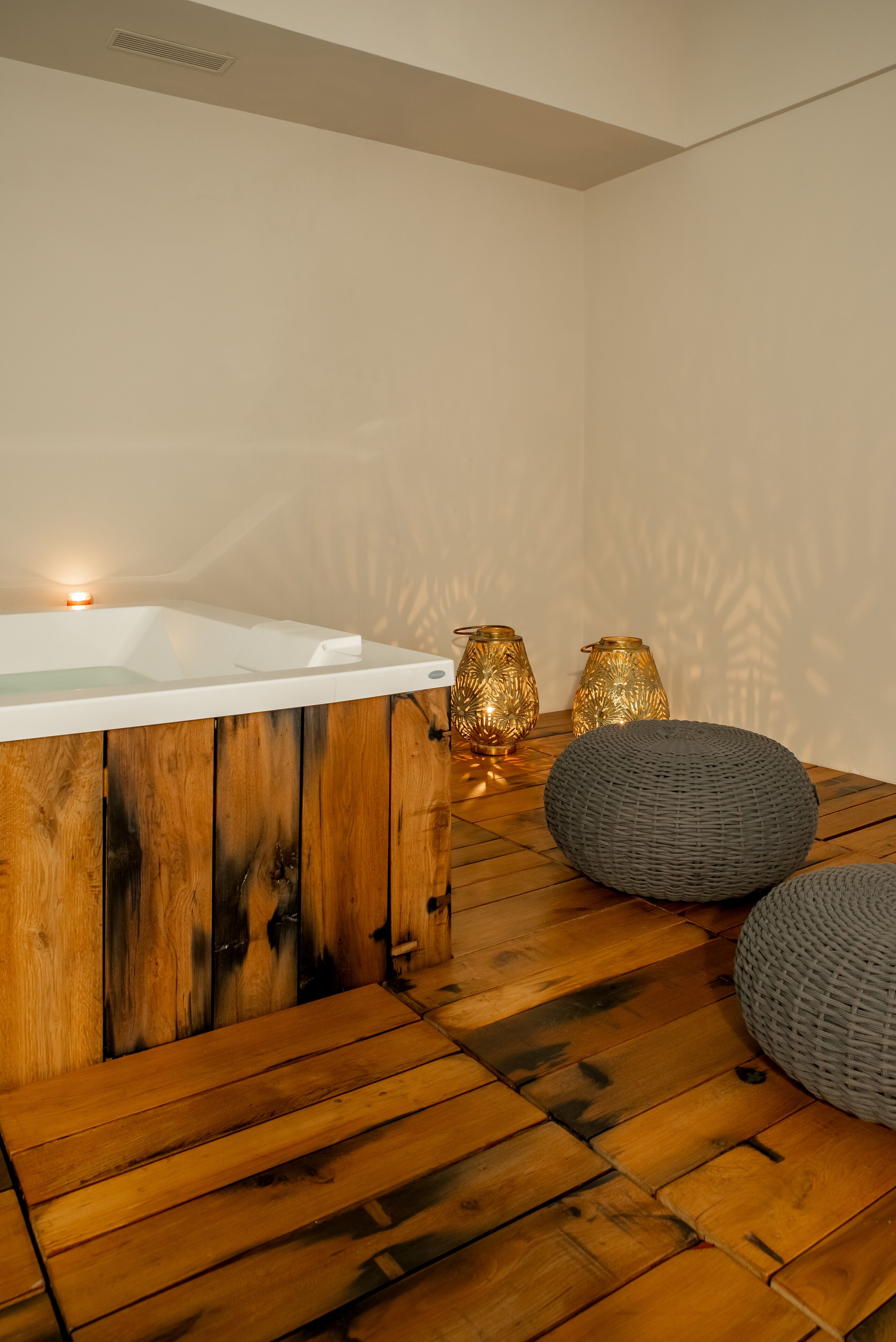 Un suelo de madera con una bañera blanca, dos lámparas doradas y dos poufs grises.