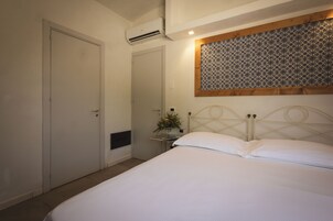 A bedroom with a bed, a door, an air conditioning unit, a small table with a vase, and a patterned wall above the bed.