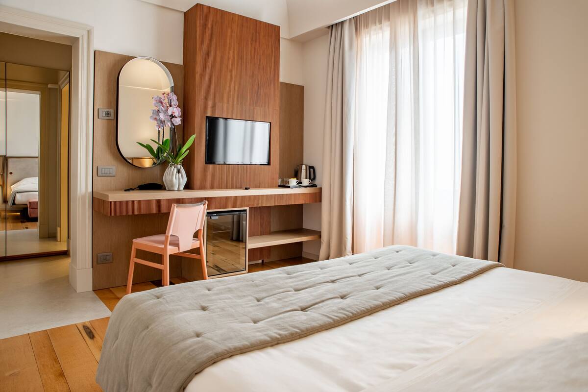 A hotel room with a large bed, a desk with a chair, a television, and a mirror.