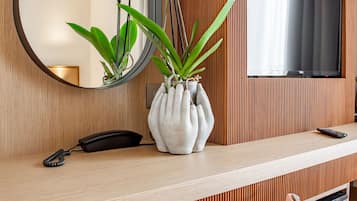 Ein modernes Hotelzimmer mit einer Wand aus Holzpaneelen, einem großen Spiegel, einem Flachbildfernseher, einer Vase mit Orchideen, einem Telefon und einem rosa Sessel.