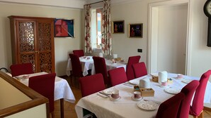 Un comedor con sillas tapizadas en rojo, manteles blancos y un mueble de madera con paneles decorativos.